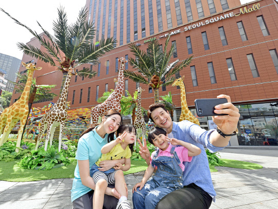 24일 서울 남대문로5가 서울스퀘어 앞 야외광장에 전시한 야생동물 모형 앞에서 가족 고객들이 기념촬영을 하고 있다. <서울스퀘어 제공>